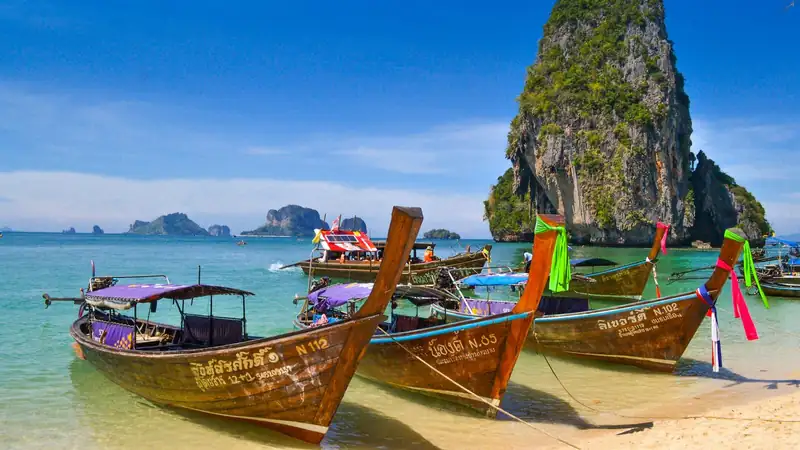Longtail boats on a turquoise beach beneath limestone karsts, southern Thailand