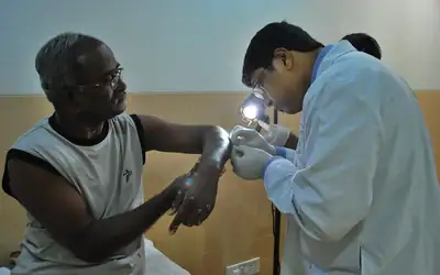 Doctor examining an elderly patient's hand with a penlight during a follow-up