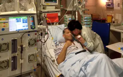 Patient resting in an intensive care bed beside monitoring and dialysis equipment