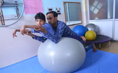 Physiotherapist guiding a young patient through a balance exercise on a gym ball