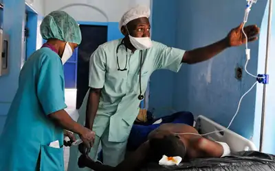 Clinicians adjusting an IV drip for a patient on a hospital ward in Africa